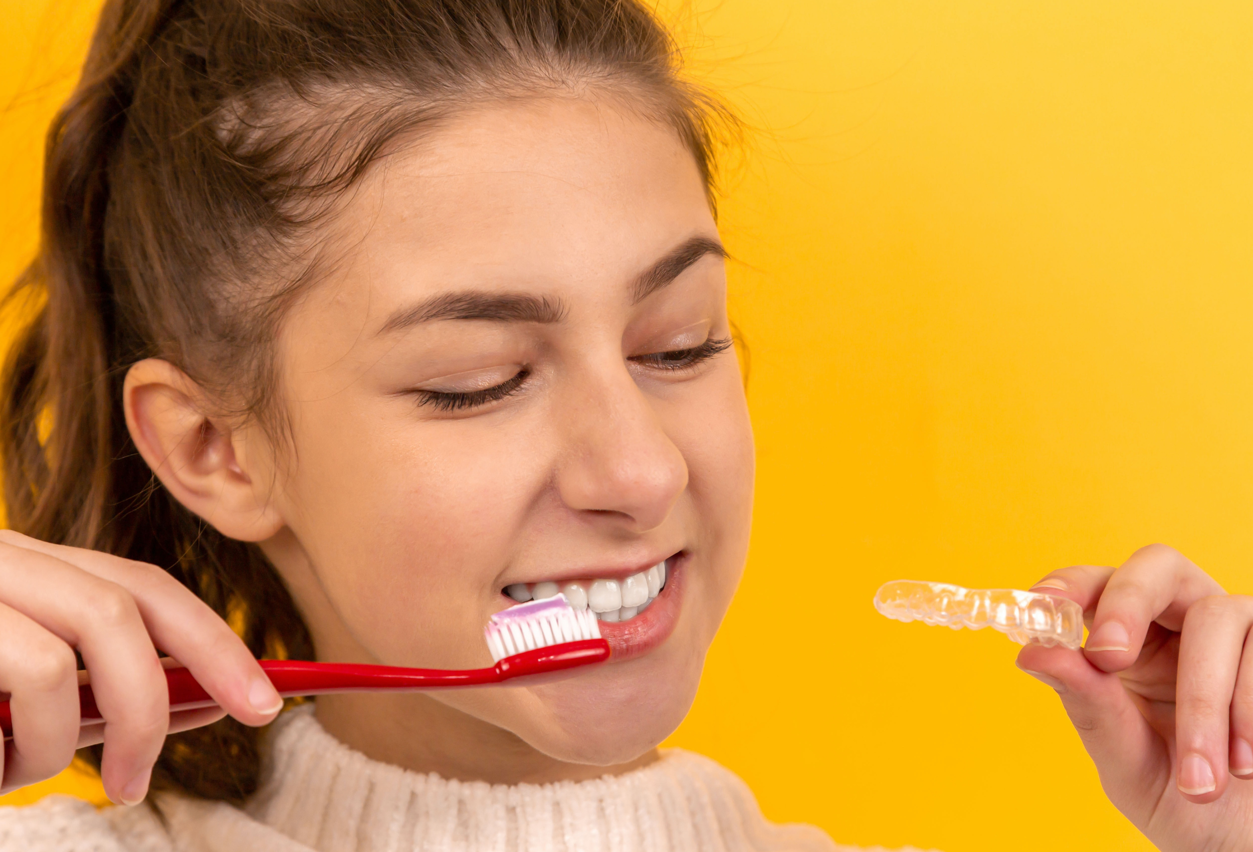 teen holds toothbrush for braces and an invisalign tray