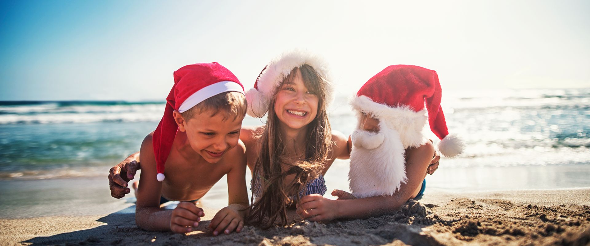 kids wearing santa hats lay on beach and talk stocking stuffer ideas