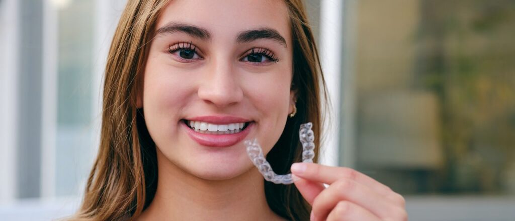 Smiling woman holding Invisalign aligner, demonstrating orthodontic treatment options.